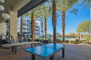 Un'area all'aperto con tavolo da ping pong, posti a sedere e palme.