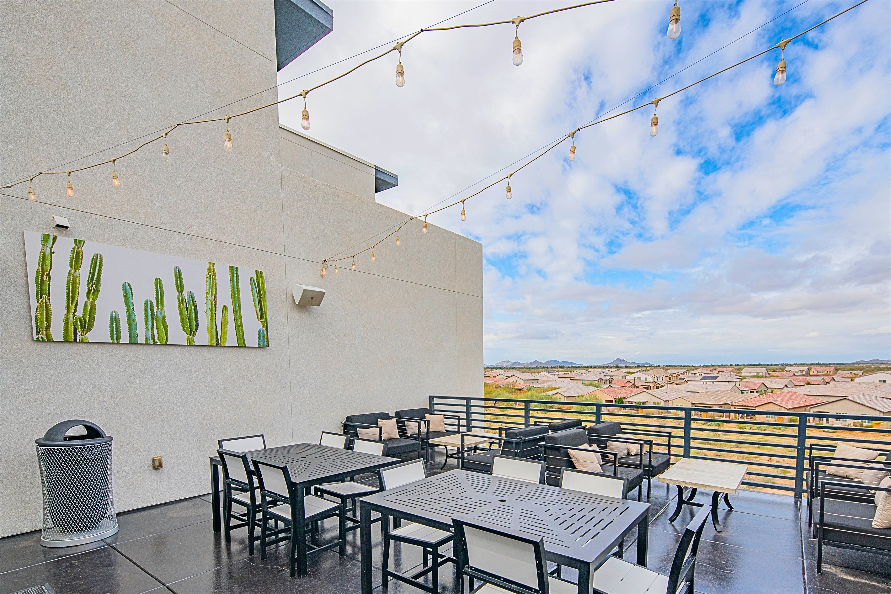 Eine Außenpatio-Terrasse mit Tischen, Stühlen, Lichterketten und einer Kakteen-Kunst am Wand.