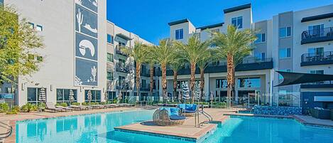 A modern hotel with a swimming pool, palm trees, and lounge chairs.