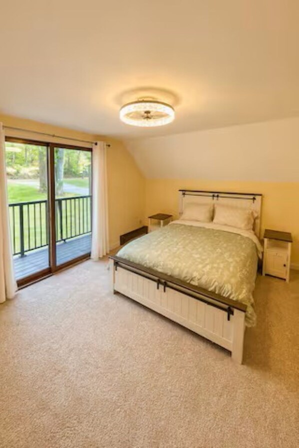 A bedroom with a bed, a nightstand, a ceiling light, and a sliding glass door leading to an outdoor area.