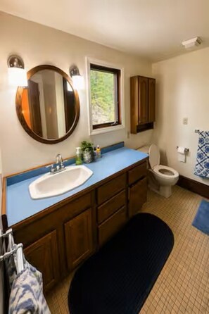 A bathroom with a sink, mirror, window, toilet, and wooden cabinets.