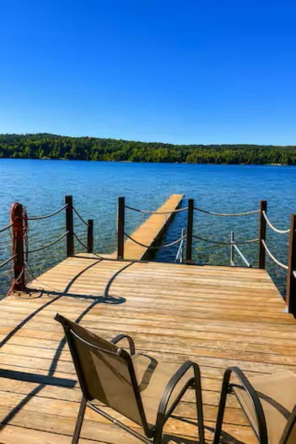 A wooden dock extending into a lake with a clear view of the water and a forested shoreline.