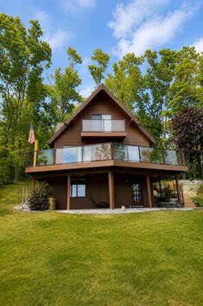 A two-story house with a flat roof, large windows, and an American flag. - Lakefront 3-Bedroom Retreat on Huffman Lake (Elmira)