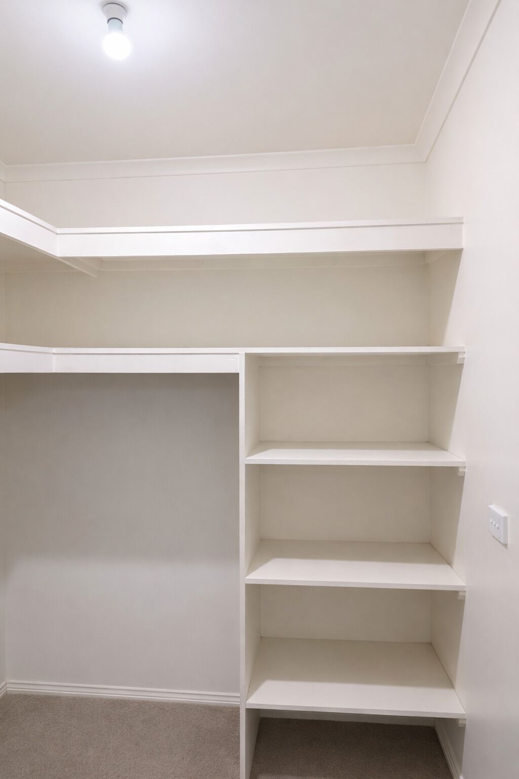 Ein Zimmer mit integriertem Kleiderschrank, mehreren Regalböden und einer Deckenleuchte.