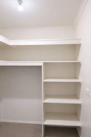 A room with a built-in closet featuring multiple shelves and a ceiling light.