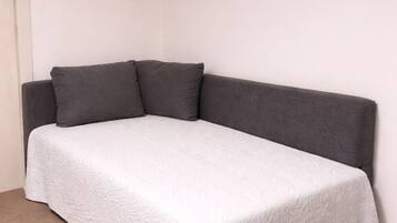 A single-bed room with a grey headboard and a white bedspread.