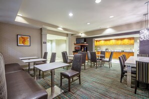 A hotel dining area with tables, chairs, a sofa, a kitchen in the background, and a framed picture on the wall. - 1BR King Sofa | Marriott Salisbury | Extended Stay, Hot Breakfast, Eastern Shore (Salisbury)