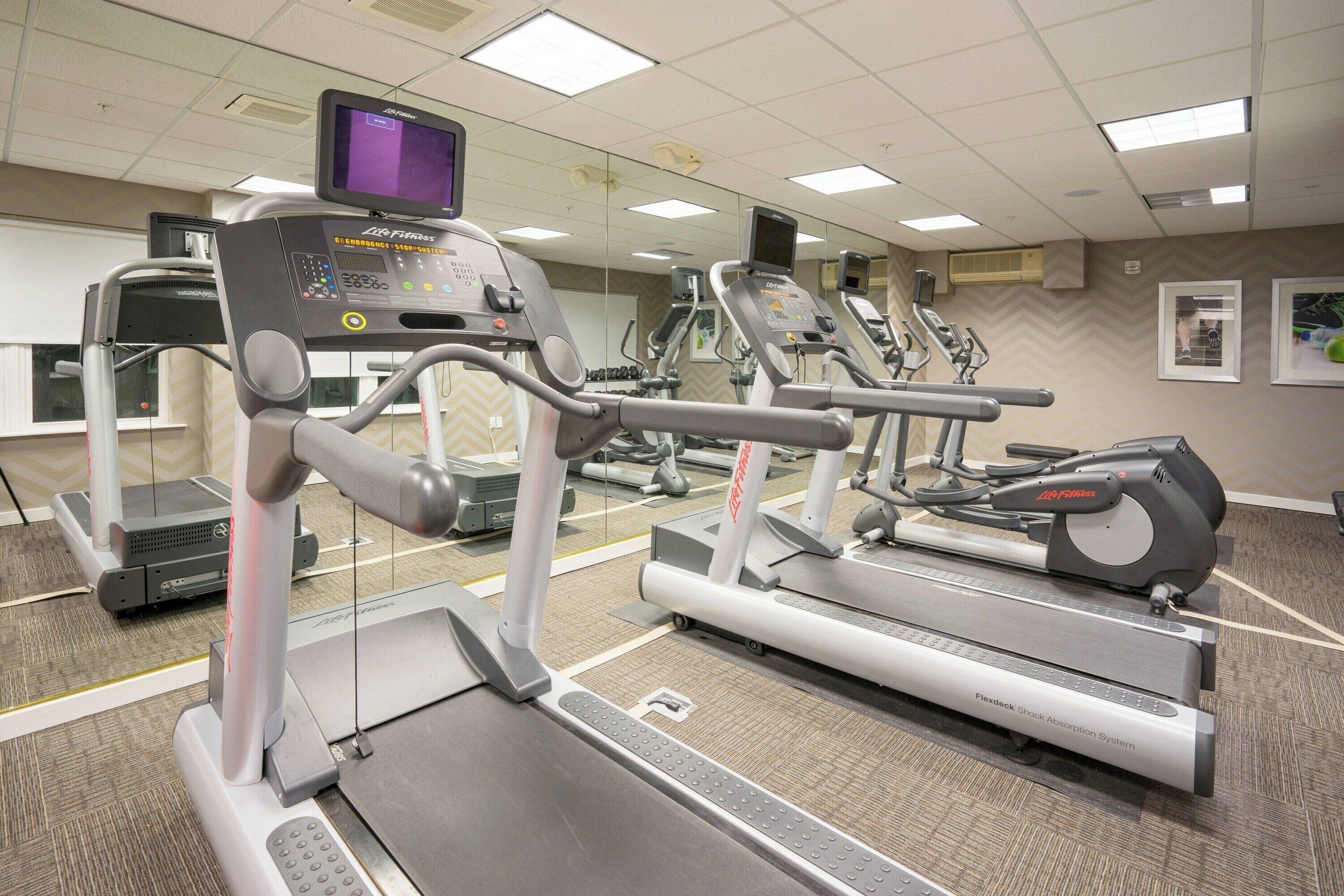 Un gimnasio con cintas de correr, elípticas y un espejo grande.