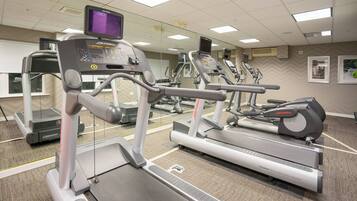 Un gimnasio con cintas de correr, elípticas y un espejo grande.