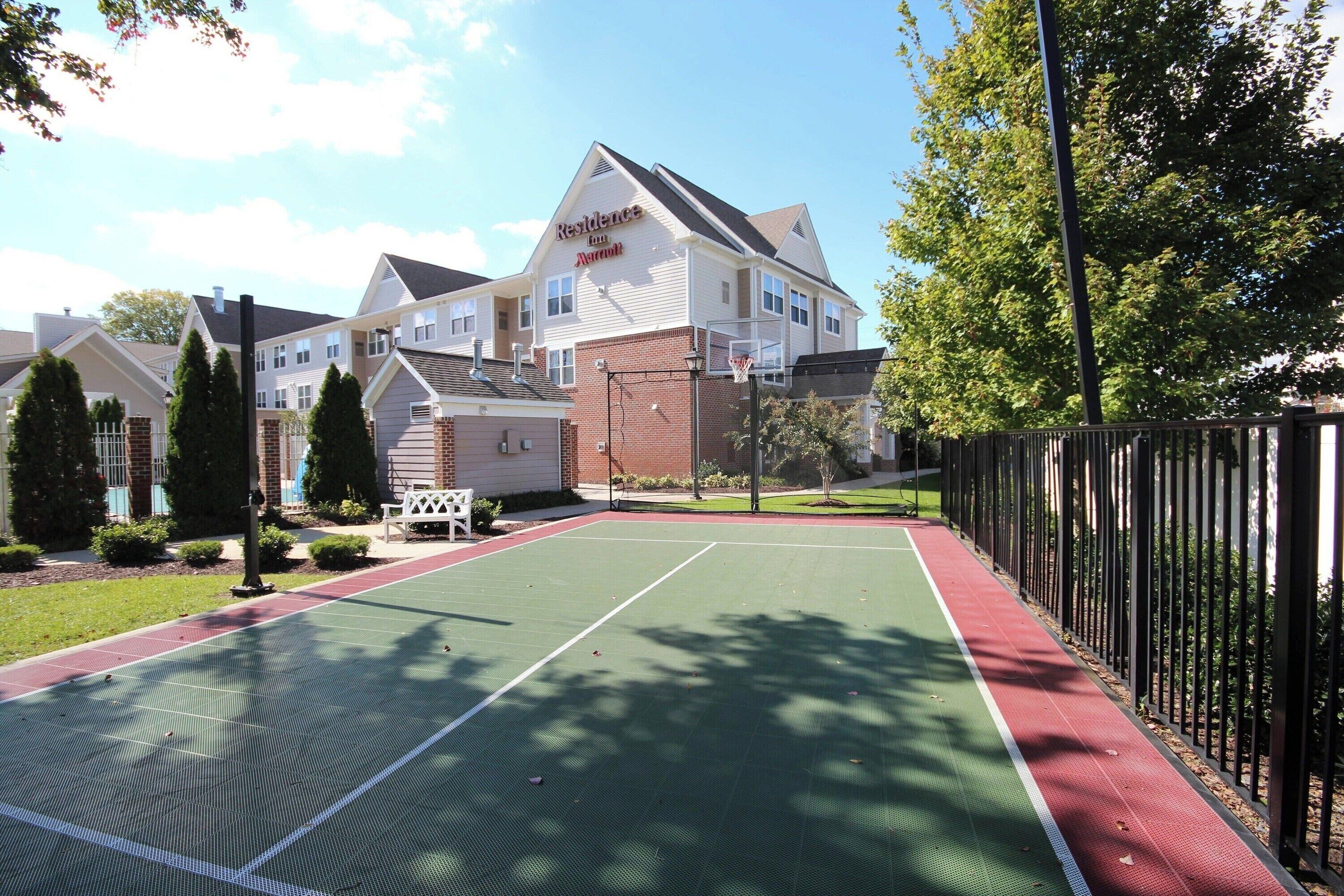 Una cancha de tenis con una valla, árboles y un edificio con un letrero que dice 'Resilience Inn & Suites'.