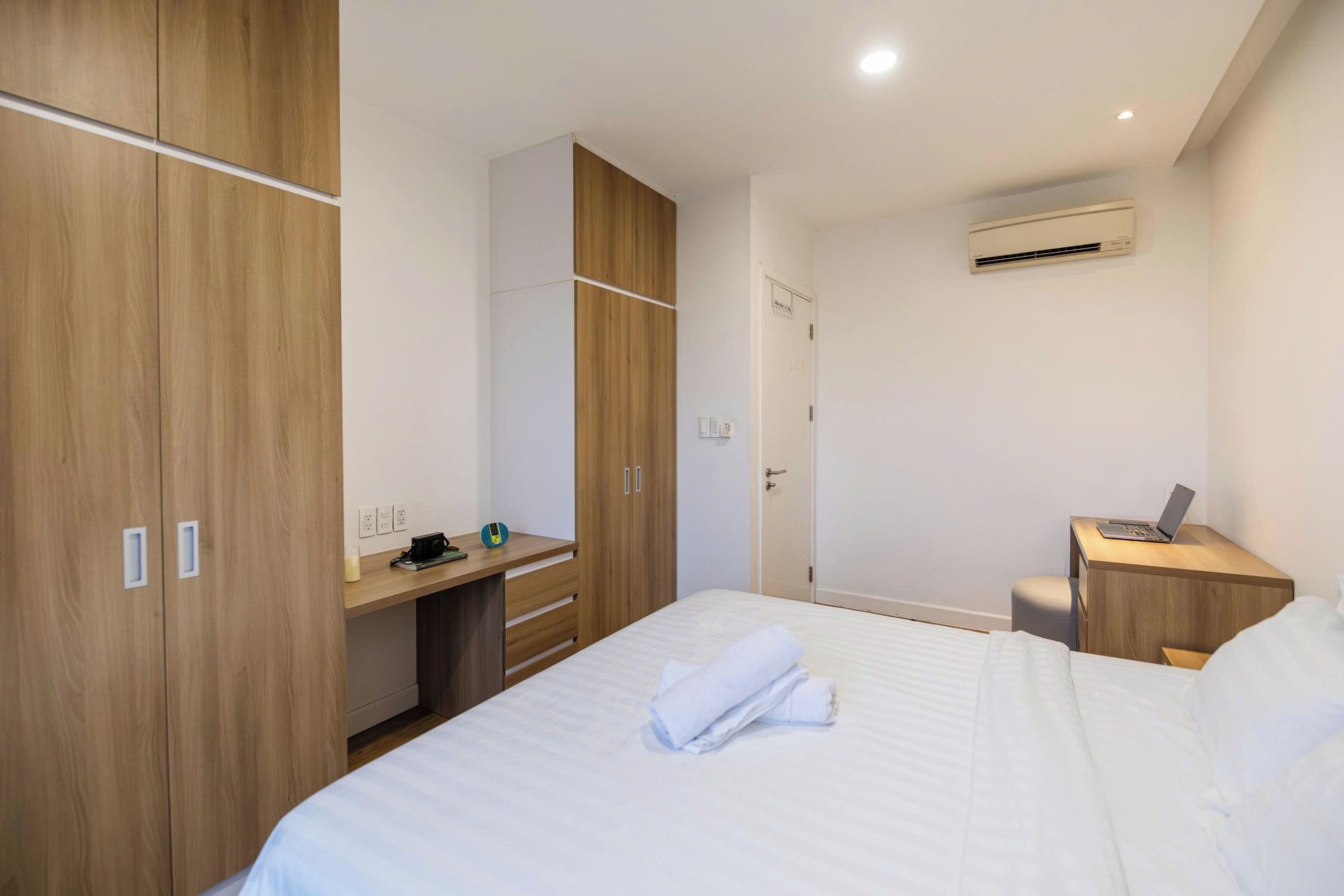 A hotel room with a bed, a desk, a wardrobe, and an air conditioning unit.
