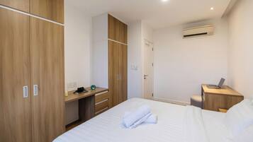A hotel room with a bed, a desk, a wardrobe, and an air conditioning unit.