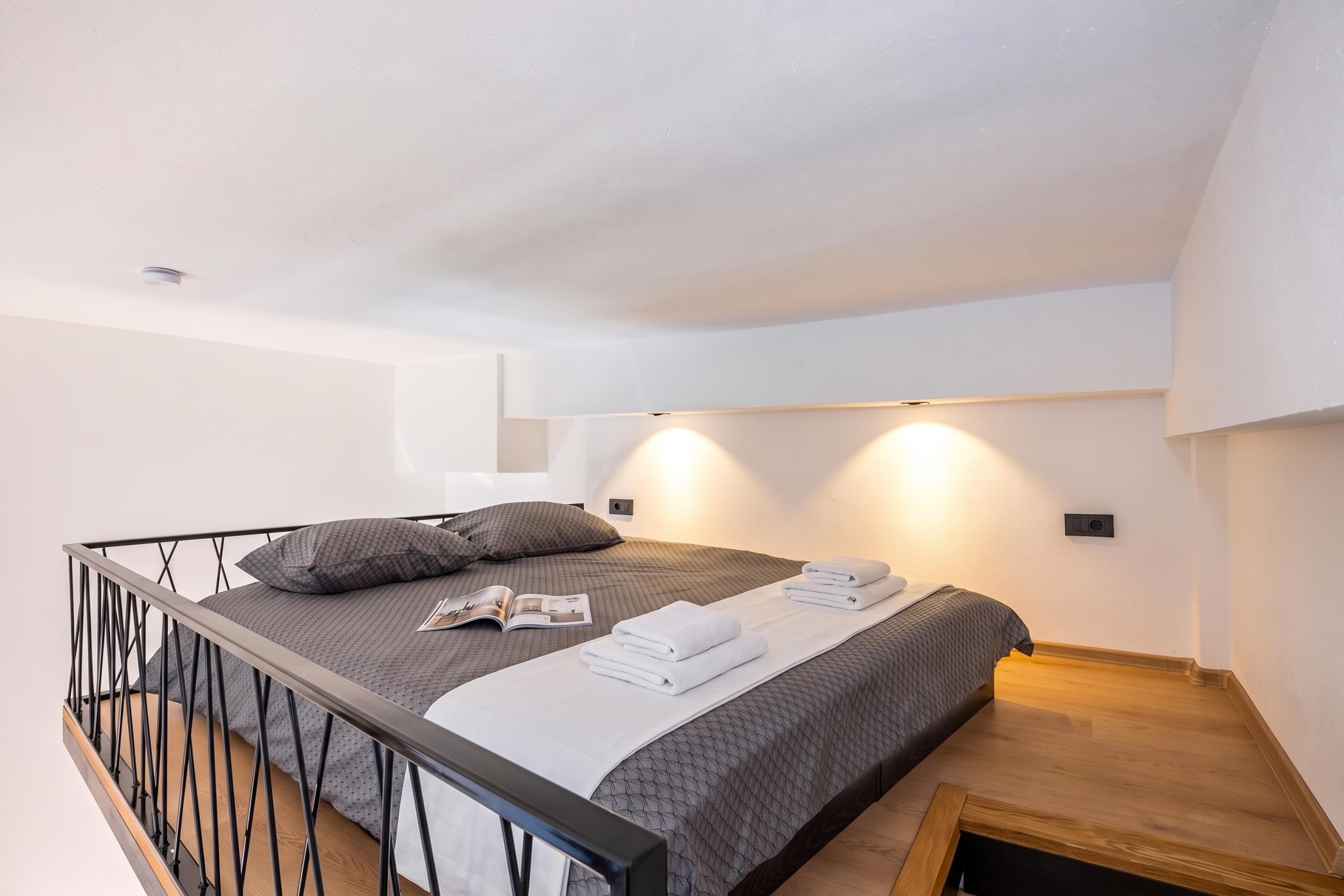 A modern bedroom with a bed, pillows, a magazine, and towels.