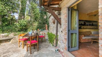 Eine Außenpatio mit einem Steintisch, Holzstühlen, einer Statue und Blick auf den Garten.