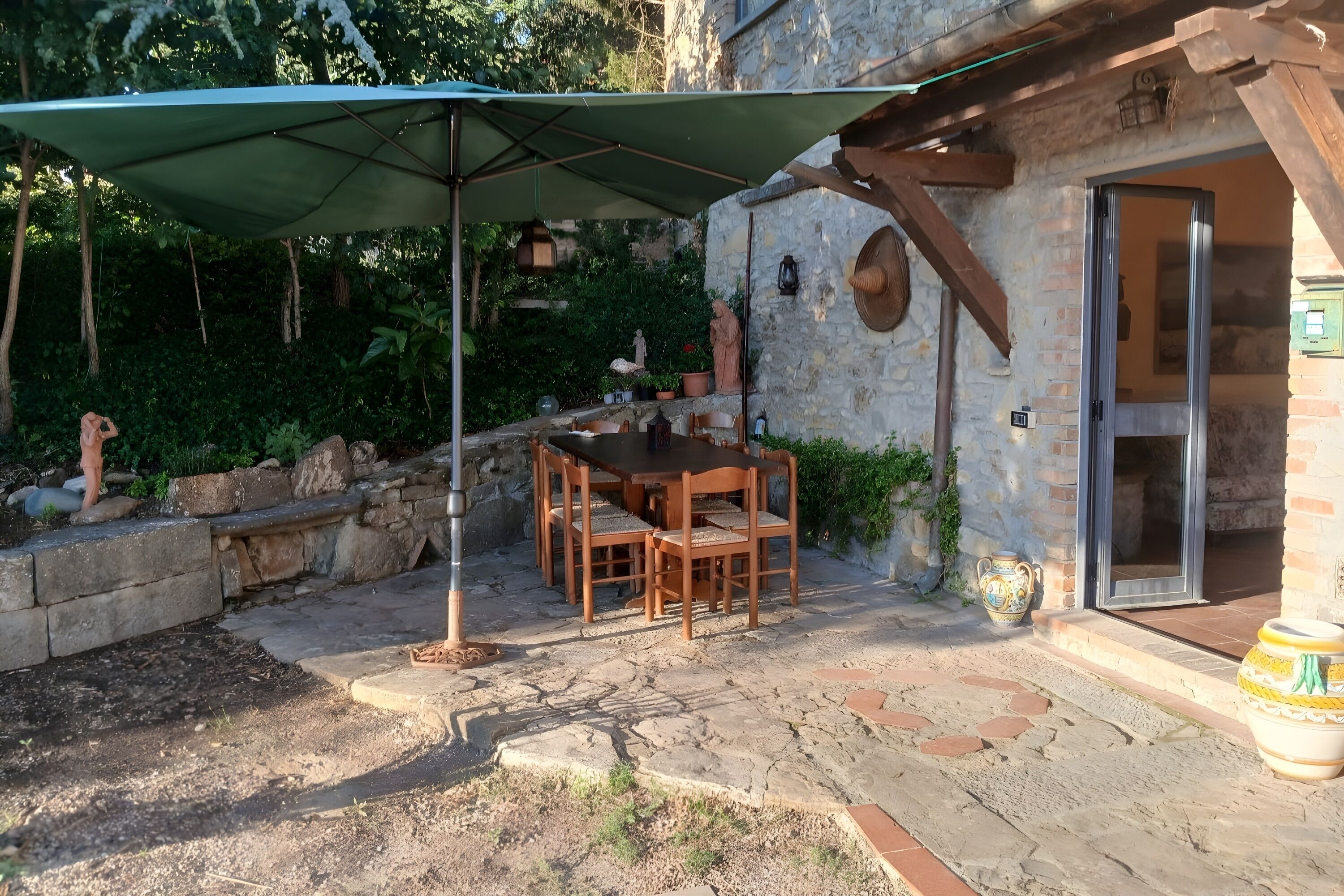 Een terras buiten met een tafel en stoelen, een stenen muur en een deur die naar een kamer leidt.