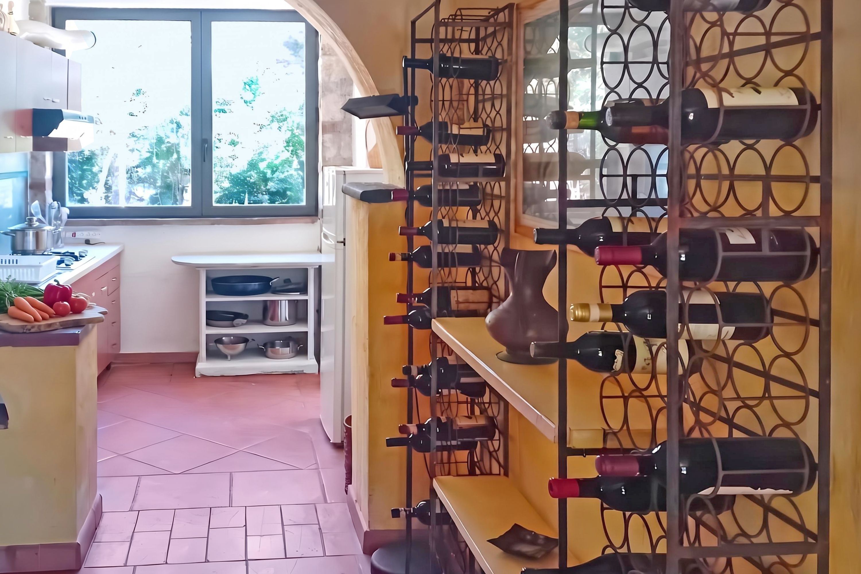 Cozinha com adega, janela com vista para vegetação e bancada com legumes.