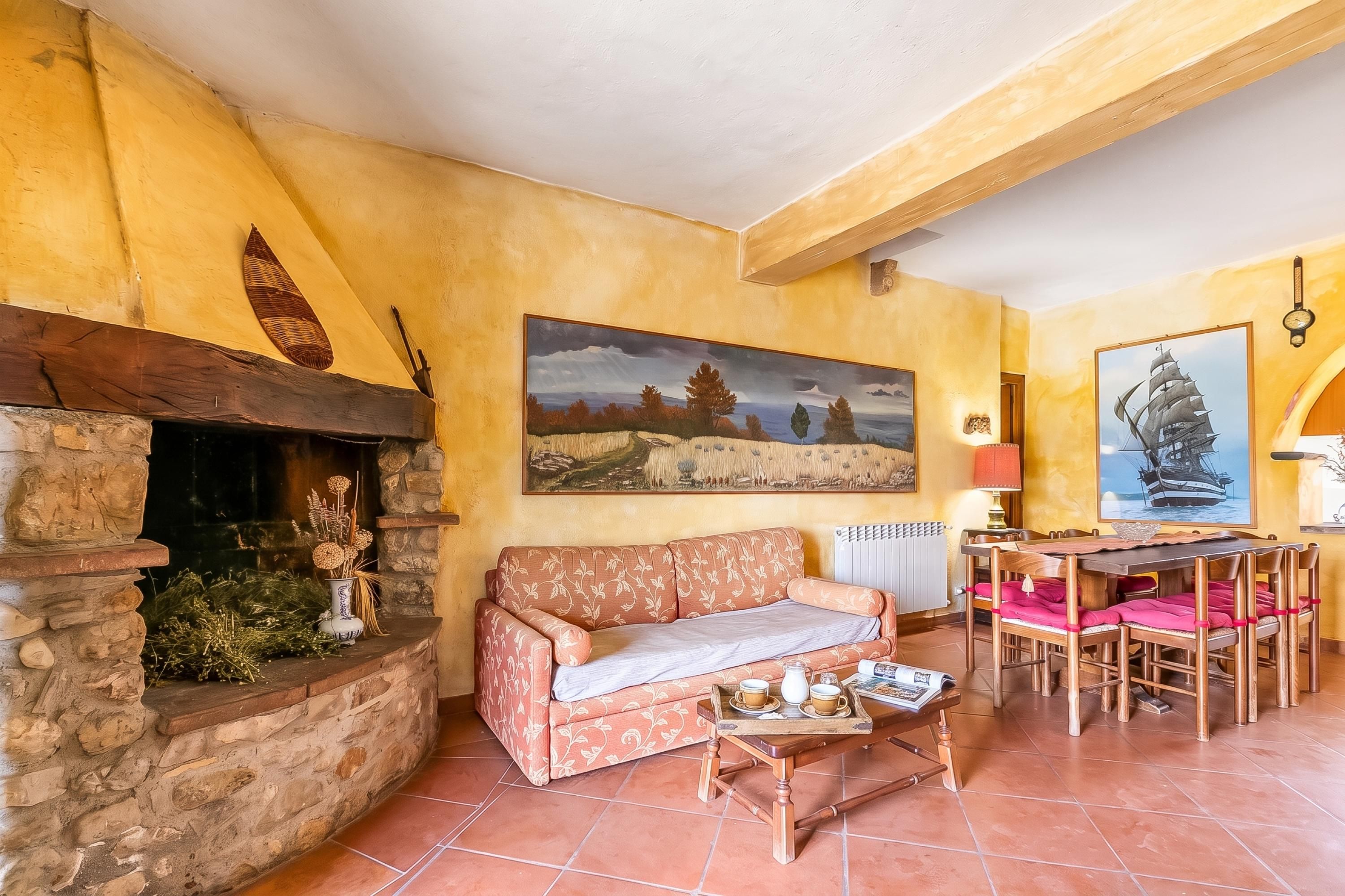 Ein gemütliches Wohnzimmer mit Kamin, einer Couch, einem Esstisch mit Stühlen und einem Gemälde an der Wand.