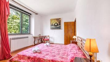 Ein Schlafzimmer mit einem Bett, einem Schreibtisch, einem Stuhl, einem Fenster mit Vorhängen, einem Bild an der Wand und einer Tür.