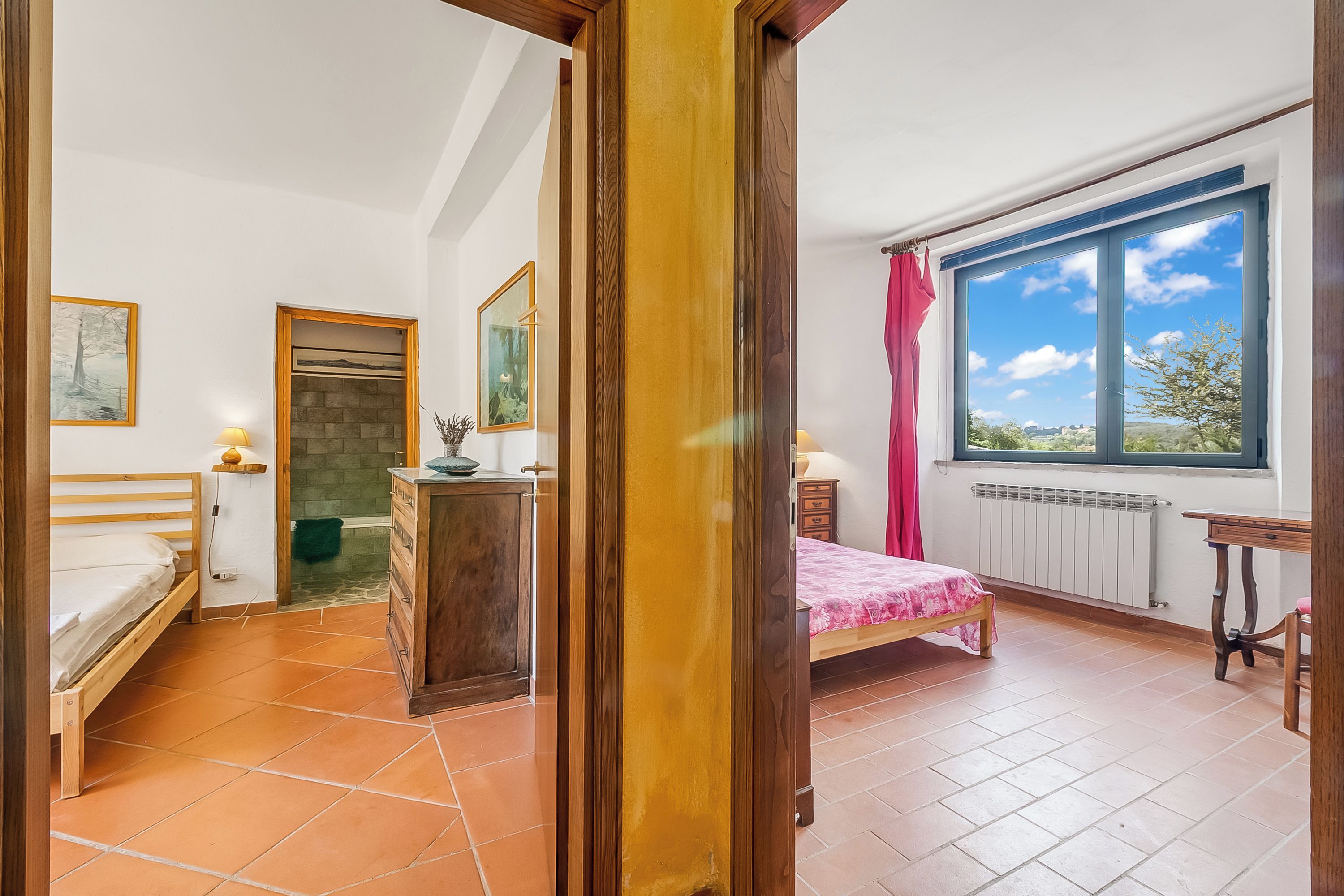 Ein Schlafzimmer mit einem hölzernen Bett, einem Schminktisch, einem Fenster mit Aussicht und einer Tür zu einem anderen Raum.