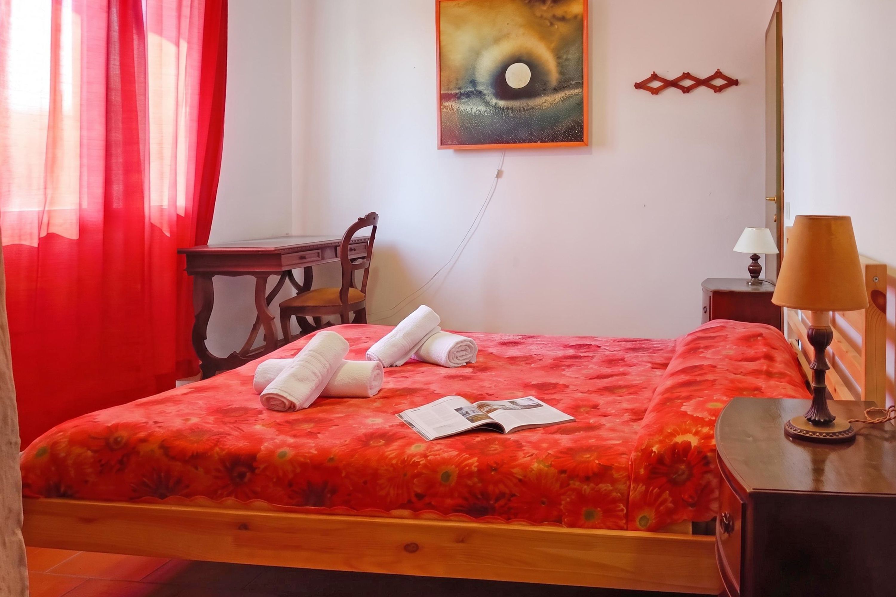 A hotel room with a bed, a desk, a chair, a lamp, and a painting on the wall.