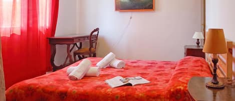 A hotel room with a bed, a desk, a chair, a lamp, and a painting on the wall.