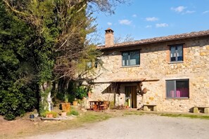 Una casa in pietra con tetto in tegole, un camino e un piccolo portico con mobili da esterno.
