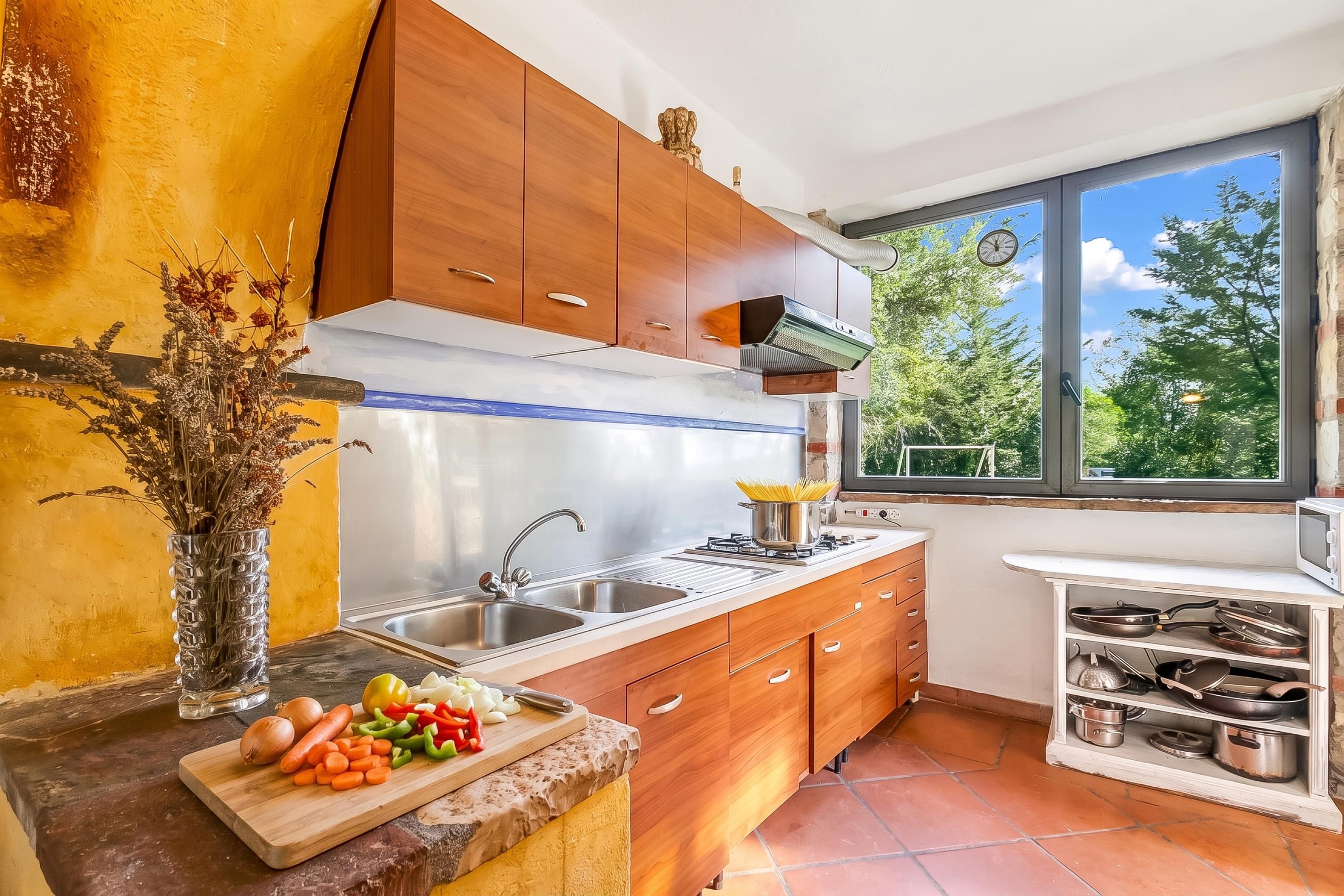 A modern kitchen with wooden cabinets, a gas stove, a sink, and a window with a view of trees.