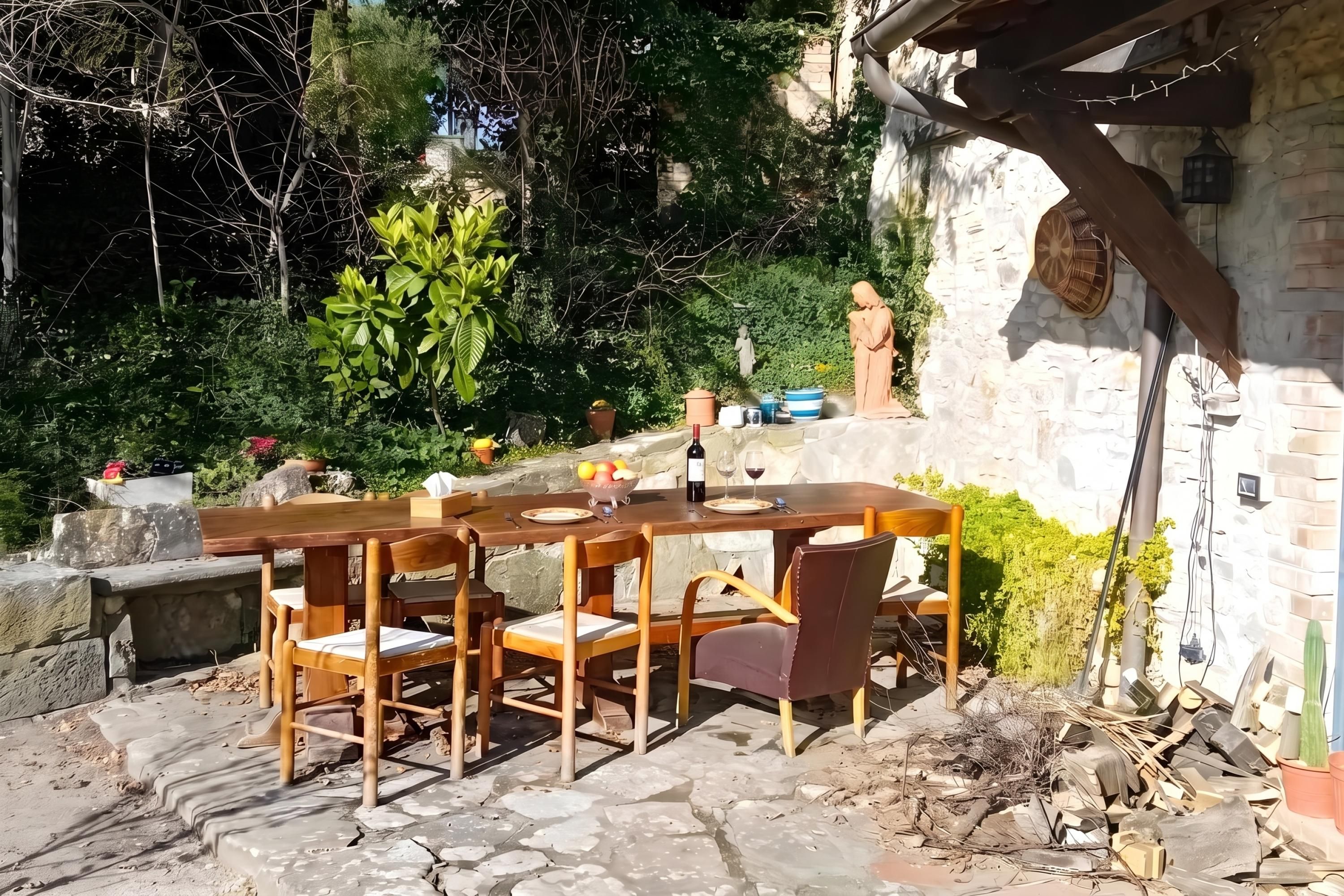 An outdoor dining area with a stone table and chairs, surrounded by greenery and a stone wall.