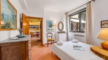 Une chambre d’hôtel avec un lit, un bureau, une chaise, une fenêtre avec des rideaux et des œuvres d’art accrochées aux murs.