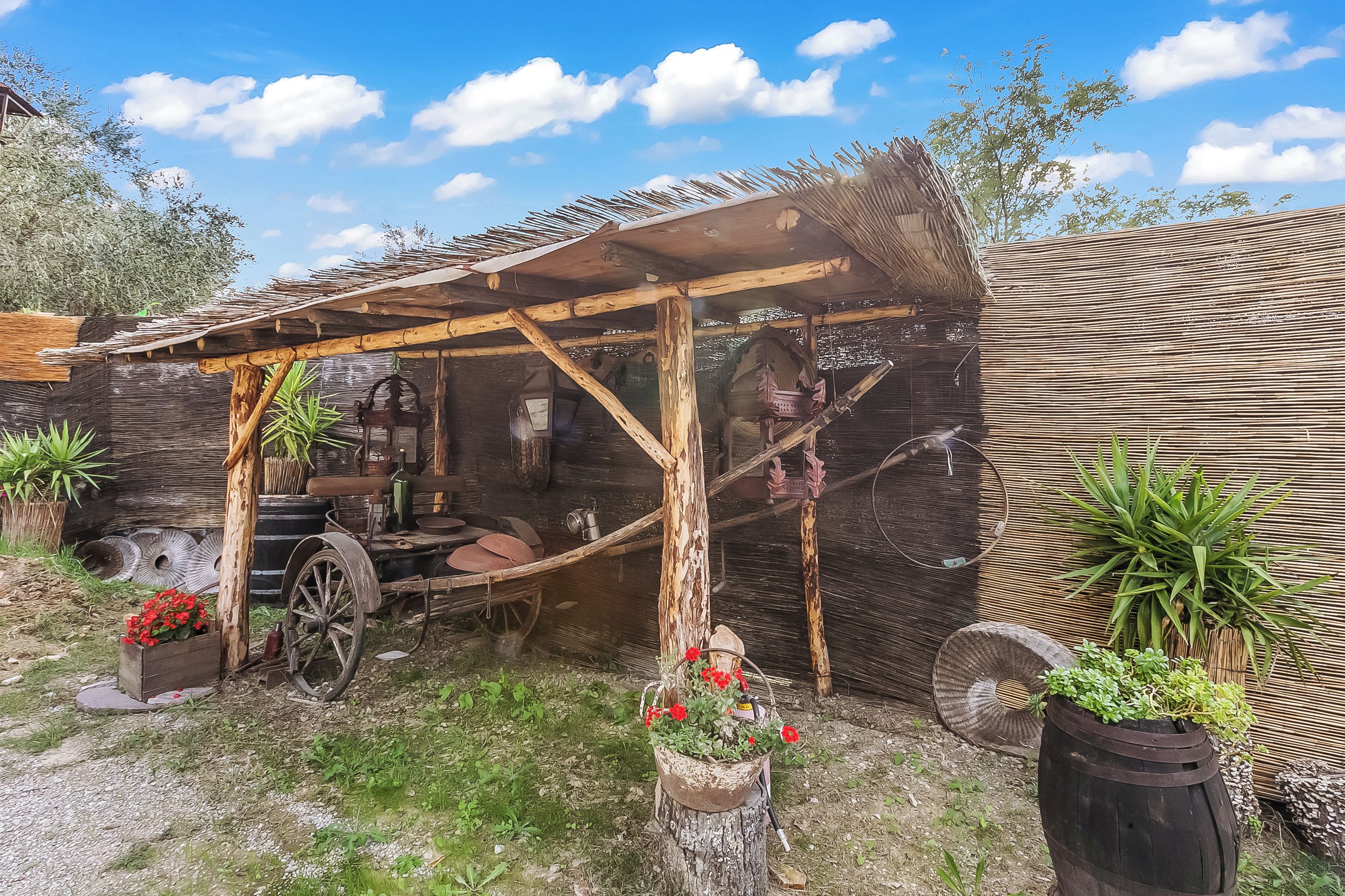 Ein rustikales Outdoor-Ambiente mit Holzkonstruktion, Schubkarre und Blumentöpfen.
