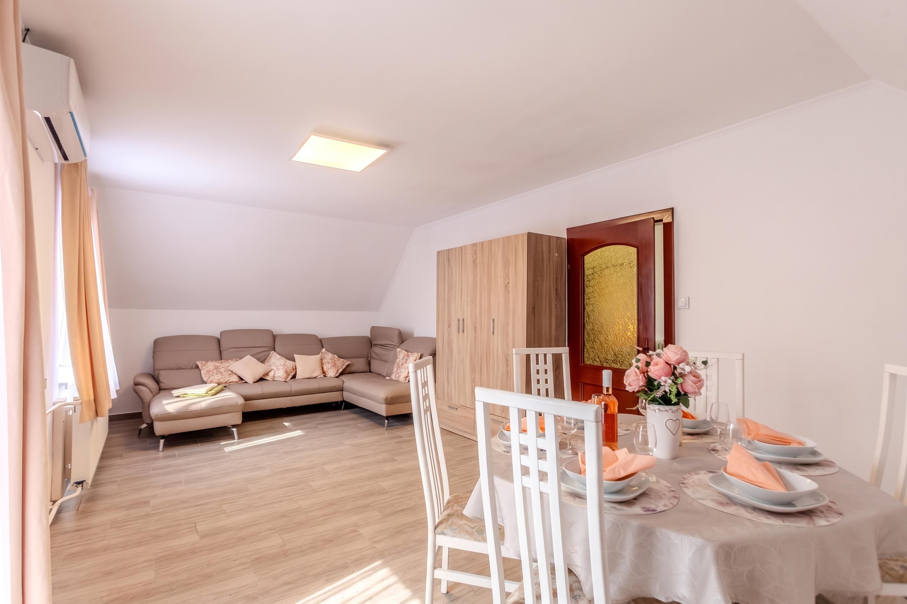 A modern living room with a sofa, dining table, and chairs. There is a wooden cabinet and a decorative mirror.