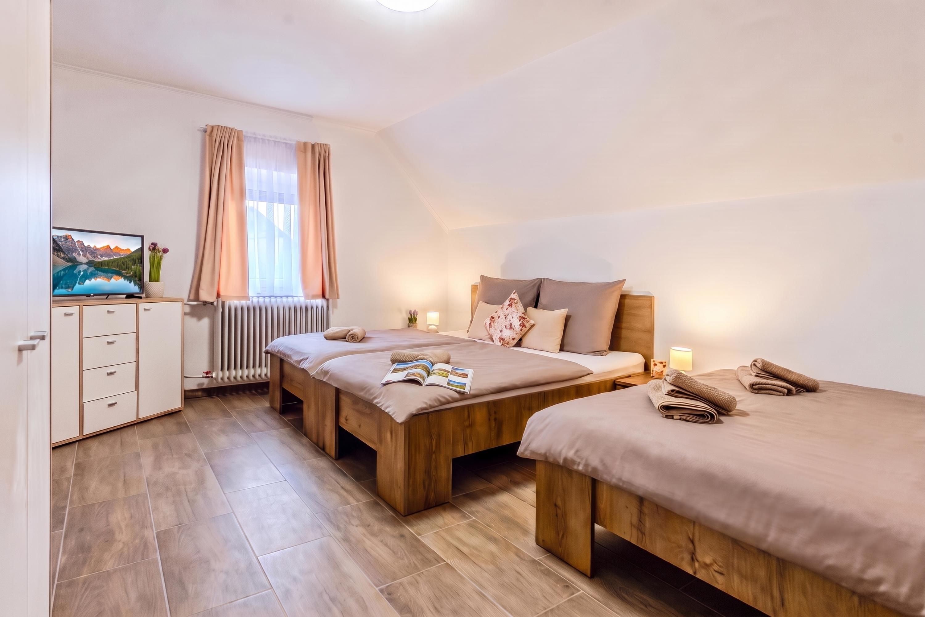 Een slaapkamer met twee houten bedden, een radiator, een televisie en een raam met gordijnen.