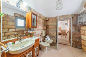 A bathroom with a stone wall, a wooden vanity, a sink, a toilet, and a mirror. - Villa Fontanelle Double Room 1, Ugento, Italy (Ugento)