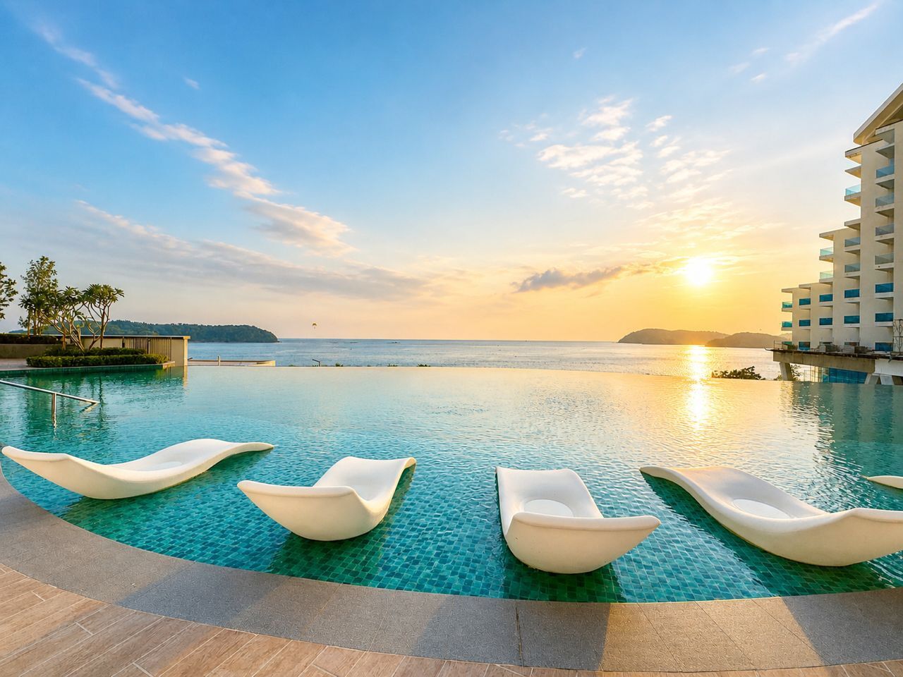 A pool with lounge chairs and a view of the ocean at sunset.