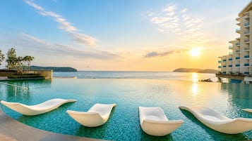 A pool with lounge chairs and a view of the ocean at sunset.