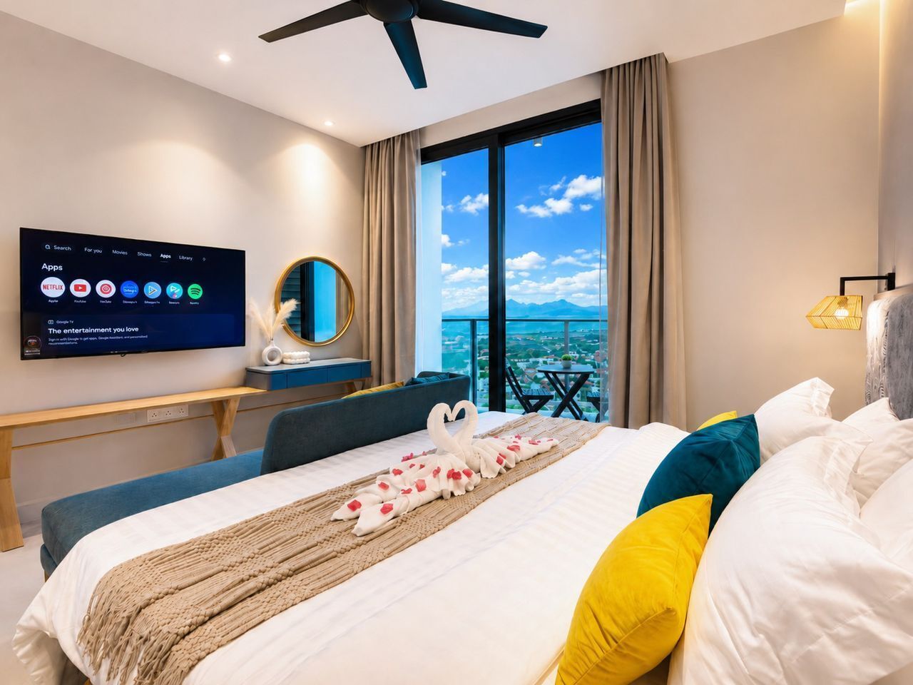 A hotel room with a bed, a TV mounted on the wall, a desk, and a view of the city through large windows.