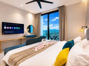 Habitación de hotel con cama, televisor montado en la pared, escritorio y vista de la ciudad a través de grandes ventanales.
