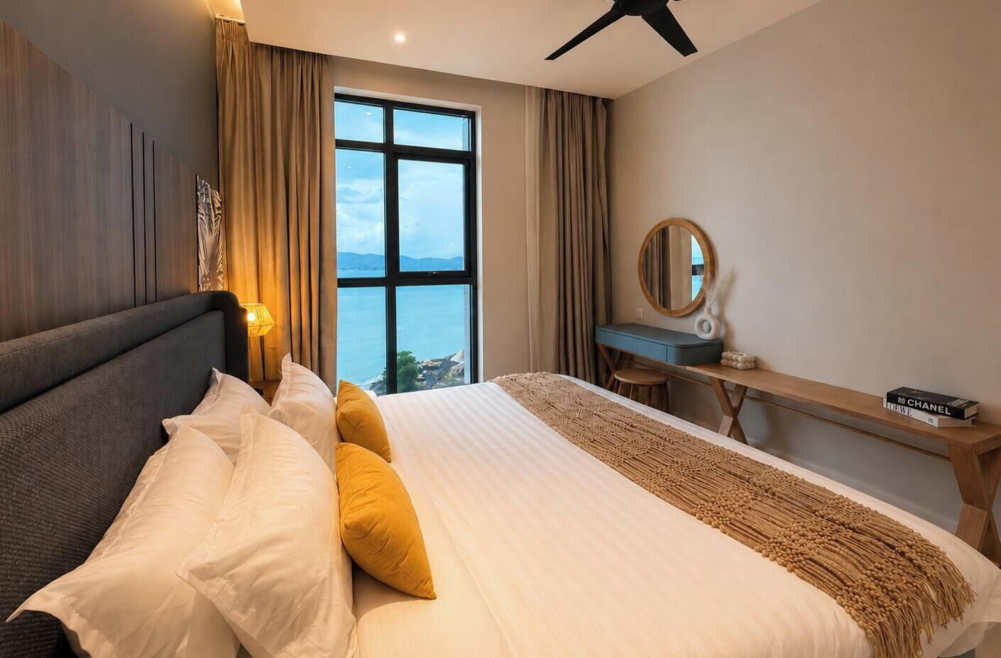 A hotel room with a bed, a desk, a chair, a large window, and a ceiling fan.