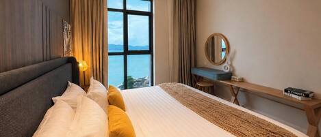 A hotel room with a bed, a desk, a chair, a large window, and a ceiling fan.