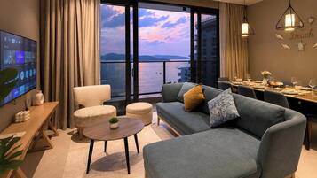 A modern living room with a sofa, armchair, dining table, and a TV.