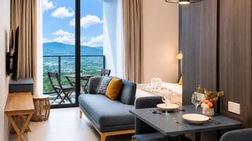 A modern hotel room with a balcony, a sofa, a dining table, and a TV.