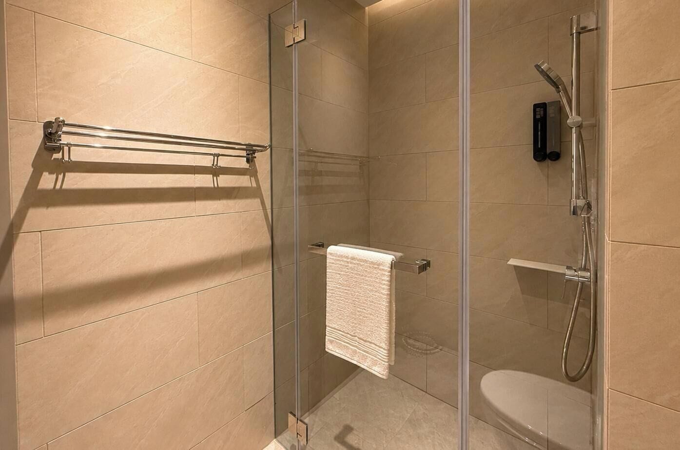 Et bruseafsnit med glasvægge, en håndbruser, et håndklædetørrestativ og et toilet.