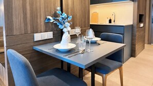Un comedor moderno con una mesa dispuesta para dos, un jarrón con flores azules y una cocina al fondo.
