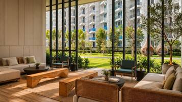 A modern living room with a sofa, coffee table, and chairs, large windows with a view of a building and greenery.