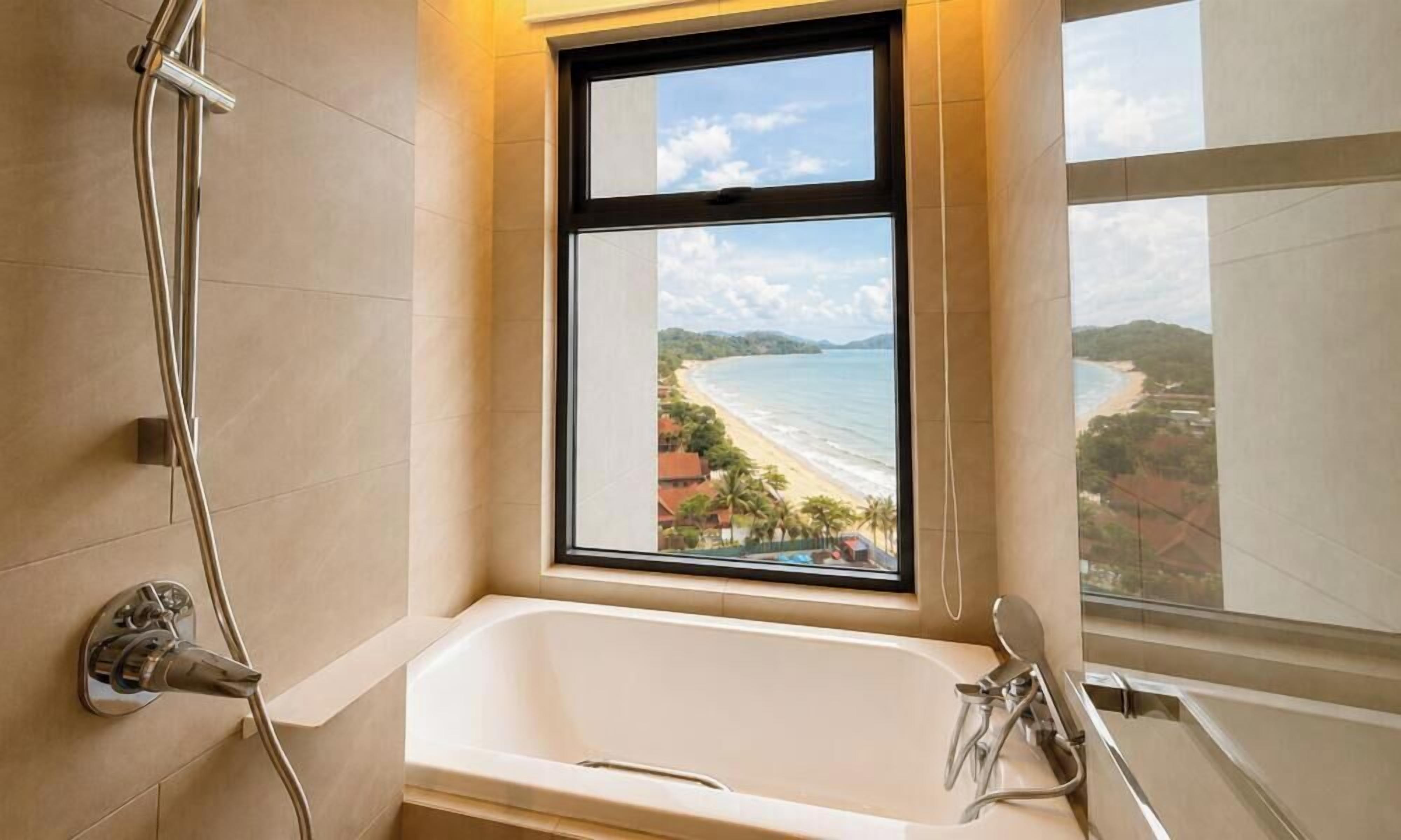A bathroom with a bathtub, a shower, and a window with a view of a beach.
