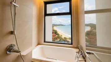 A bathroom with a bathtub, a shower, and a window with a view of a beach.