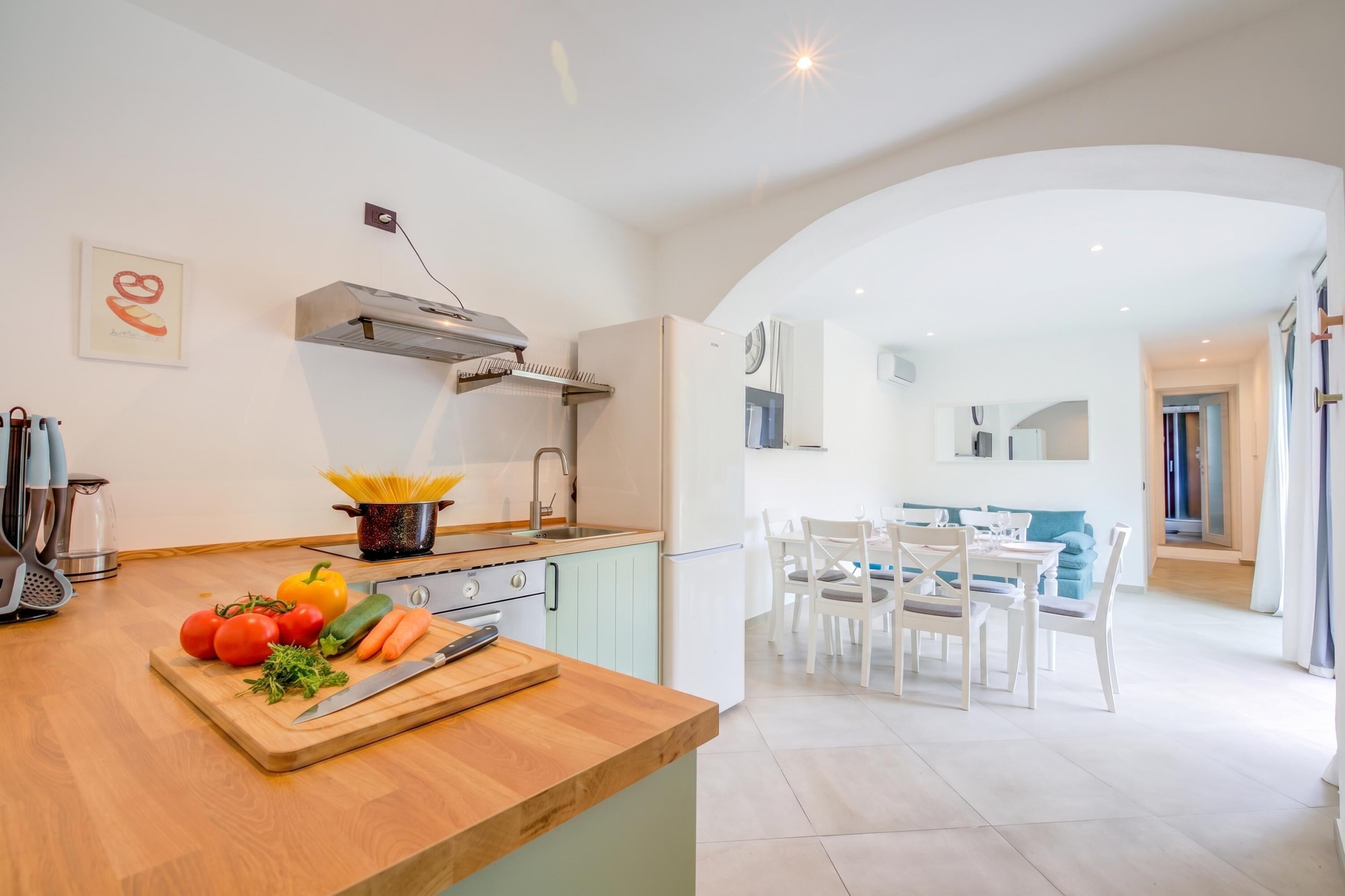 A modern kitchen with a wooden countertop, a pot of pasta, and fresh vegetables.