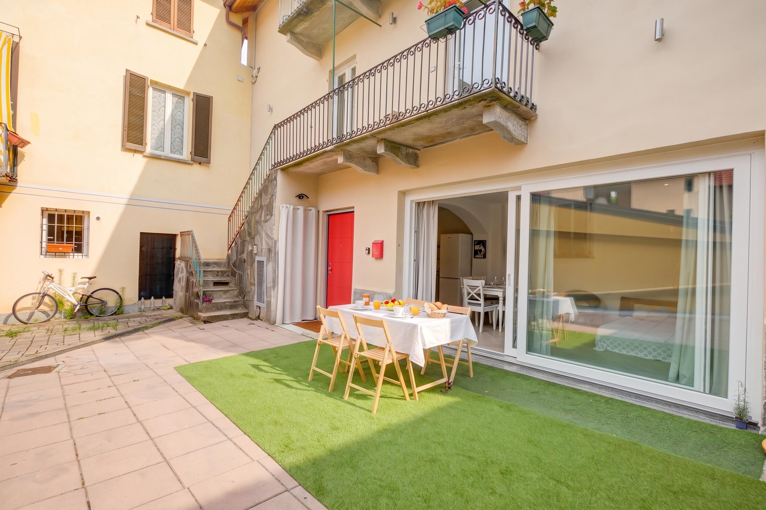 A hotel room with a balcony, a dining area with a table and chairs, and a sliding glass door leading to a kitchen.