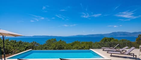 Una piscina con sillas de descanso y vista al mar.
