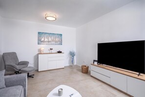 Ein modernes Wohnzimmer mit einem Flachbildfernseher, einem grauen Sofa, einer weißen Kommode und einem Segelboot-Gemälde.